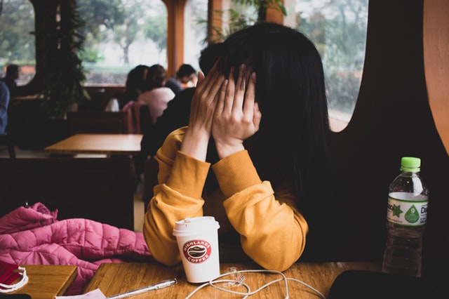 Woman covering face wearing yellow sweatshirt indoors