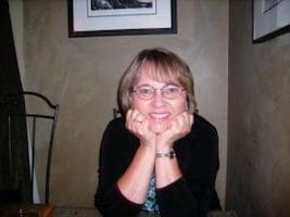 Photo of Ann Norris indoors with her chin resting on the palms of her hands