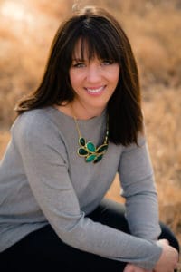 Therapist Kelly Cote outdoors in a grey long sleeve shirt and wearing a green necklace