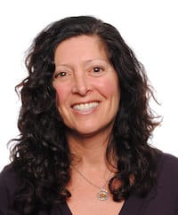 Photo of Theresa Palermo in front of a white background wearing a dark top and a necklace