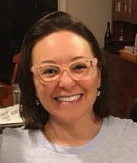 Photo of Cecilia smiling indoors wearing glasses and a white shirt