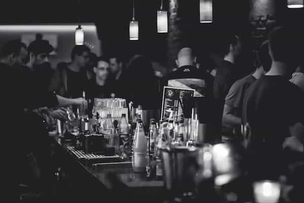 bar with drinks and many people standing around the room drinking