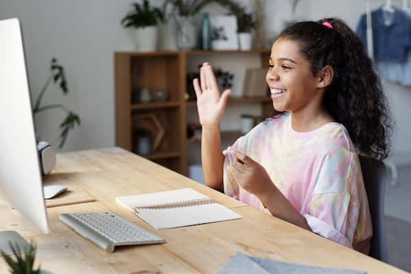 young girl sitting at desk waving at computer