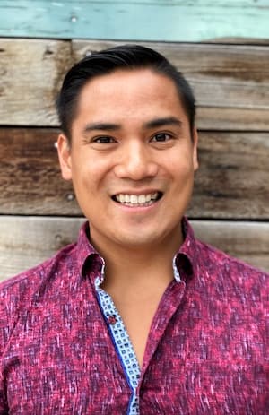 Therapist Chris Marhevka wearing a pink and purple shirt standing outdoors by wooden wall