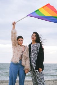 two ladys standing in front of water with lgbtqia flag