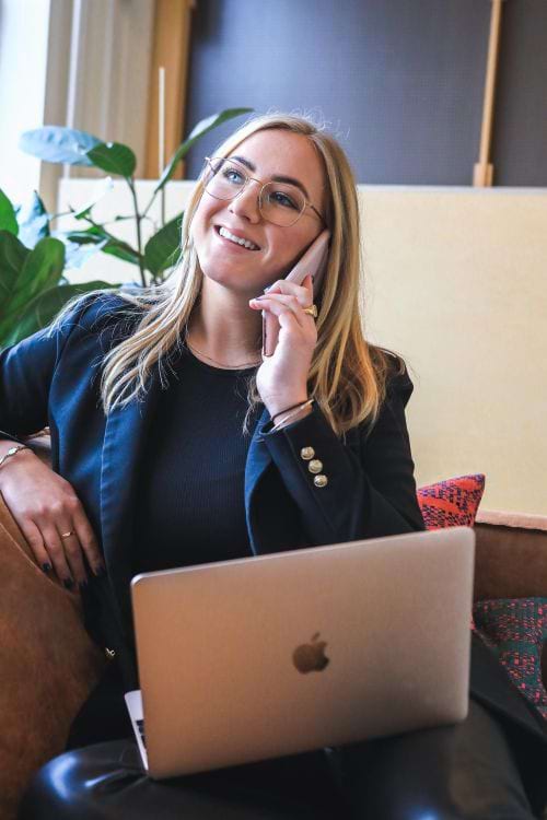 Women sitting on couch with a laptop and taking a phone call.